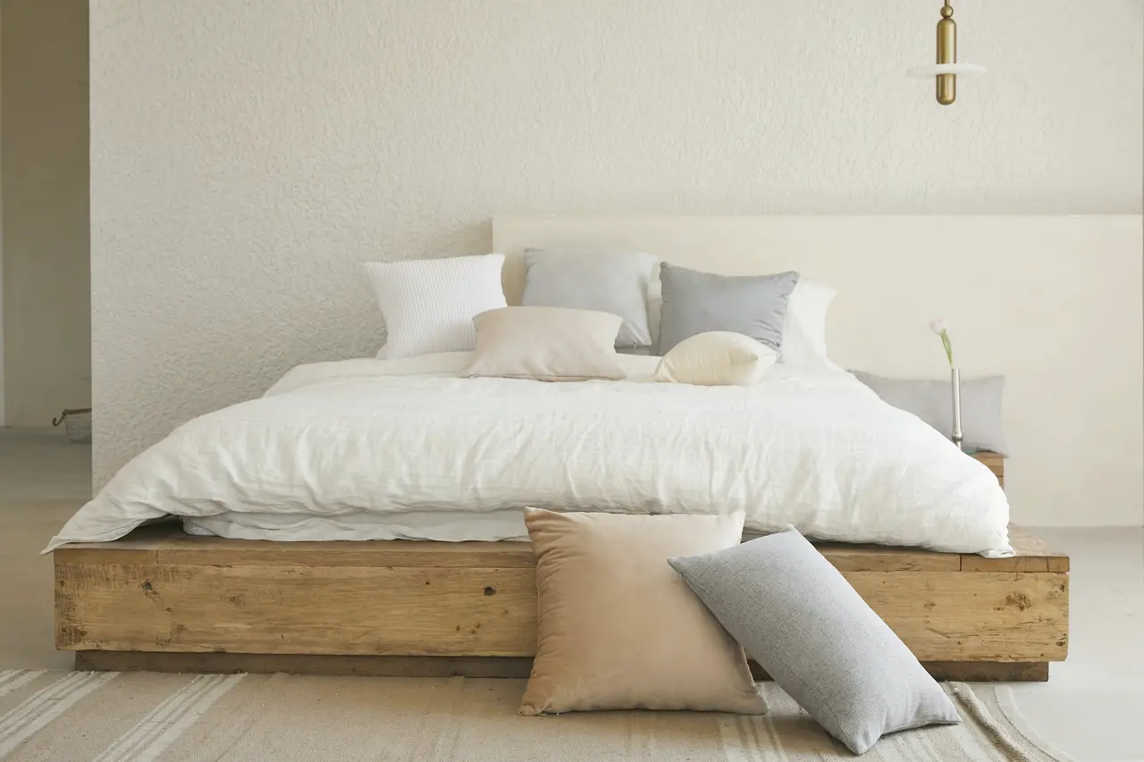 A low timber bed made up with white and oatmeal linen in a calm, sunlit bedroom